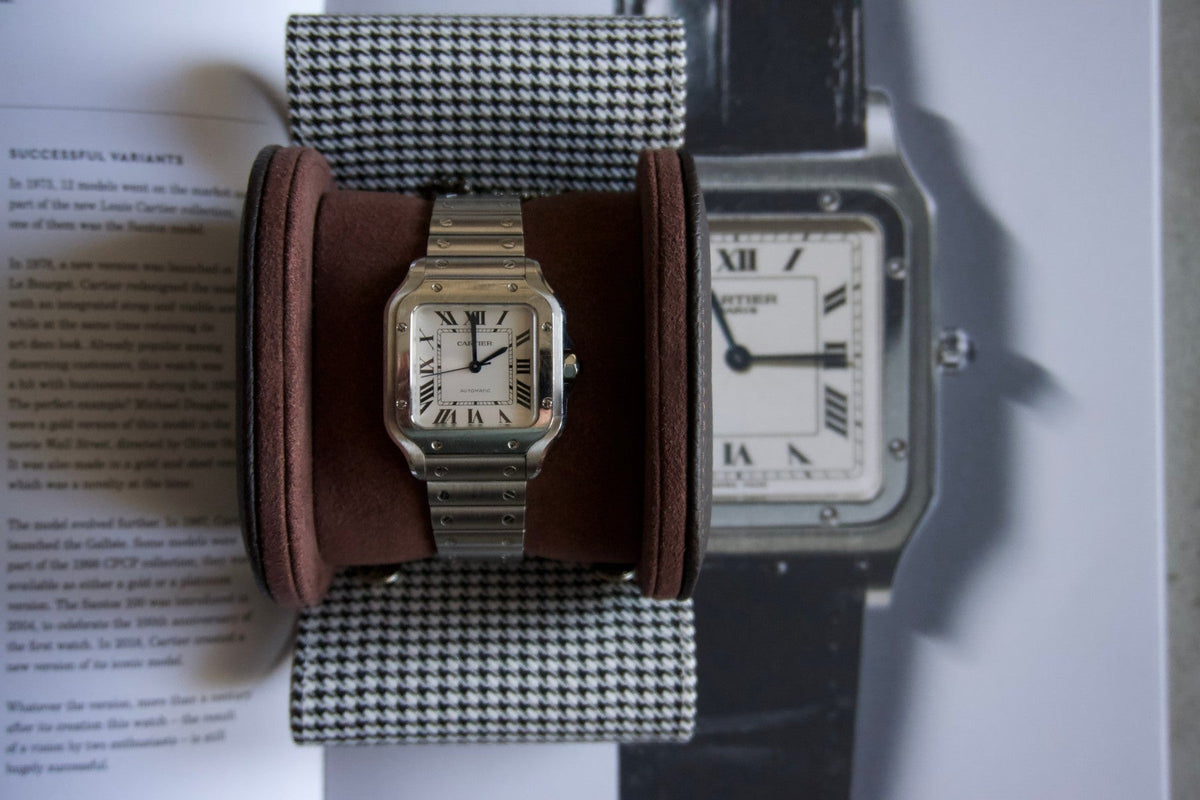 Stainless steel Cartier Santos resting in The Espresso watch roll on an open book about the Santos-Dumont
