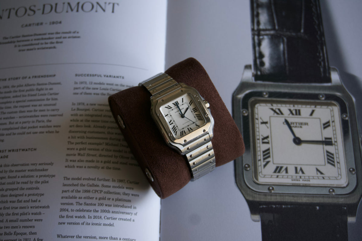 Stainless steel Cartier Santos on a suede watch pillow resting on an open book about the Santos-Dumont